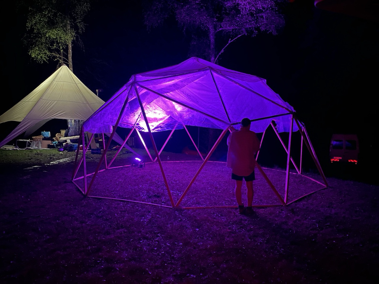 Die Kuppel bei Nacht, violett ausgeleuchtet, daneben ein Zelt
